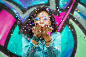 Young Black Woman blowing confetti at the camera