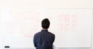 man standing in front of a white board drawing a website sitemap