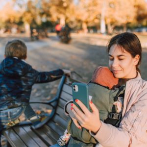 Mom looking at her phone on the playground while holding a baby