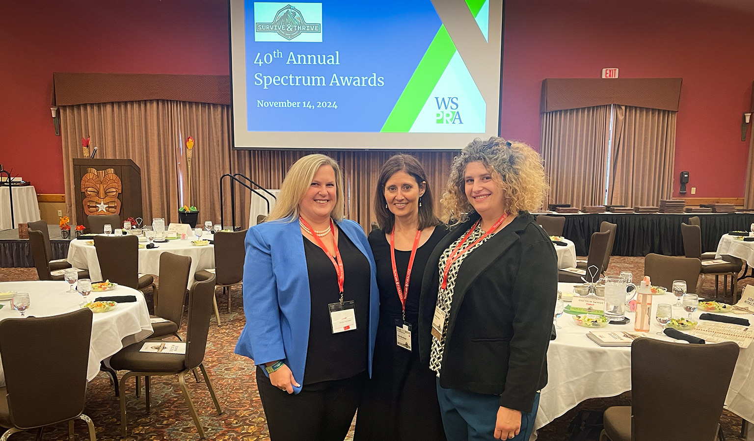 chelsea, erika and ashley smile in WSPRA main room. A screen behind them reads "40th Annual Spectrum Awards, November 14, 2024."